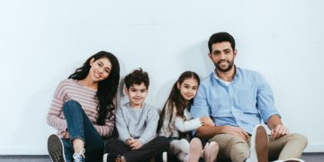 cheerful hispanic family smiling while sitting on floor near white wall