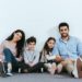 cheerful hispanic family smiling while sitting on floor near white wall